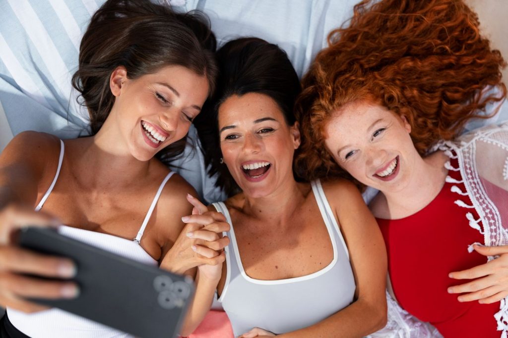 Kolme nauravaa naista ottamassa selfietä kännykkäkameralla