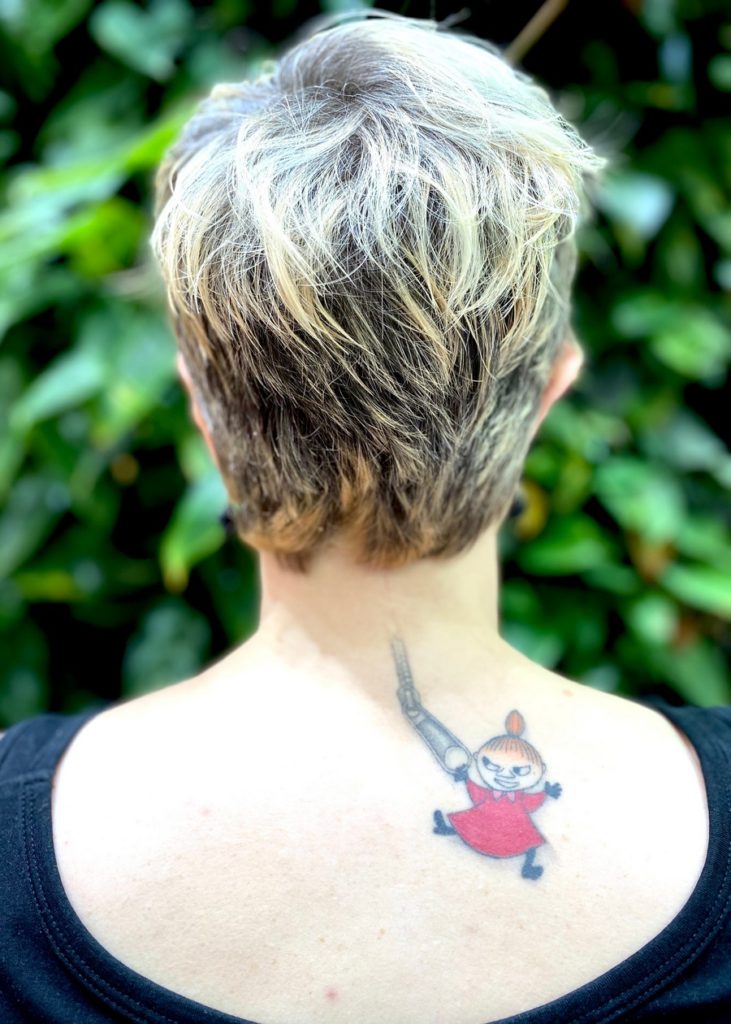 Kuvattuna naisen niska, jossa näkyy haalea arpi. Arven alapuolella on tatuointina vetoketju, jonka päässä roikkuu Muumeista tuttu Pikku Myy