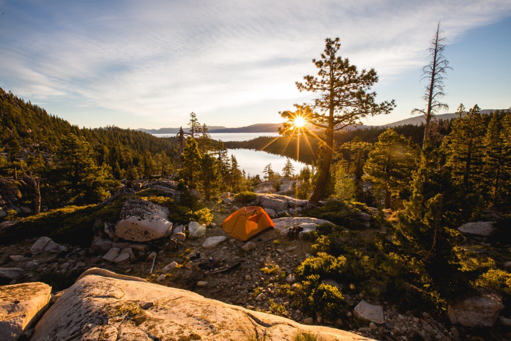 A beautiful shot of an orange tent on rocky mountain surrounded by trees during sunset