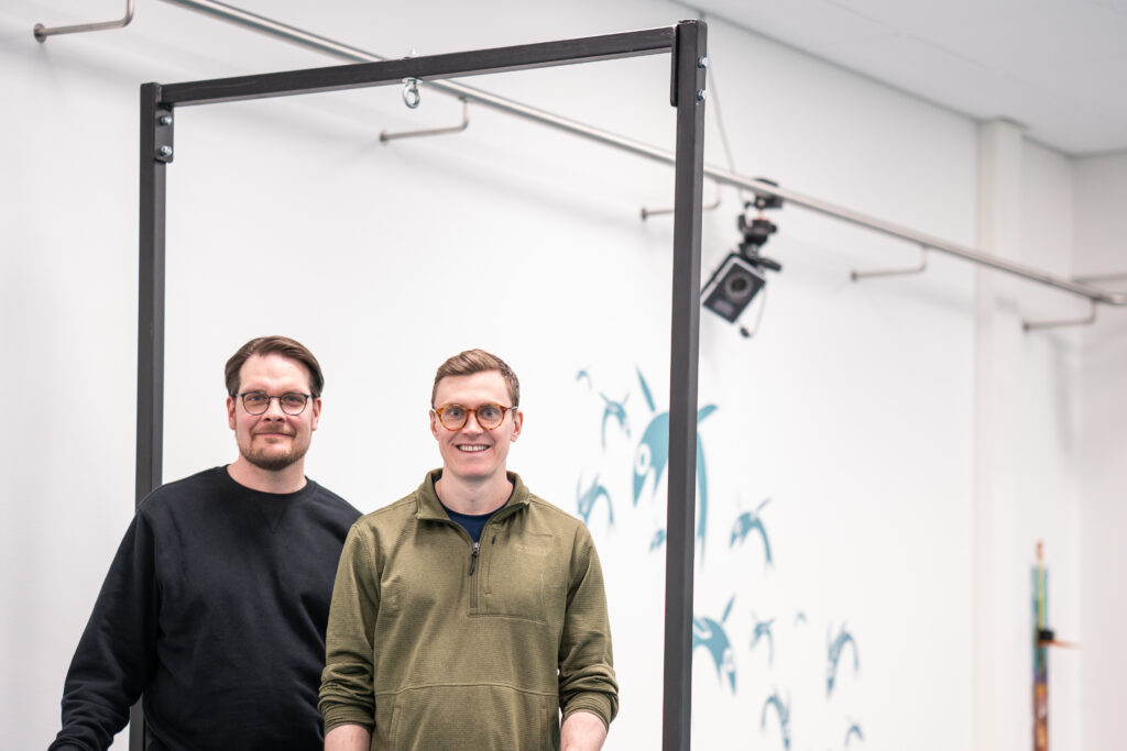 Juha-Pekka Kulmala ja Max Thurston seisovat vierekkäin vaaleassa huoneessa ja hymyilevät kameralle.