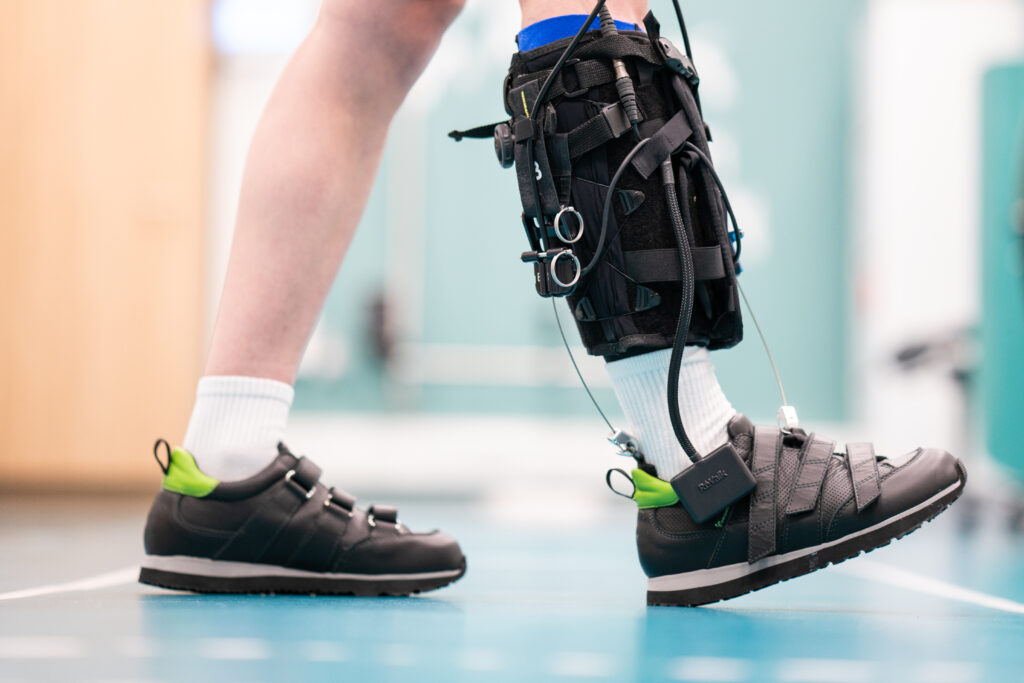 Lapsen jalat. Lapsi ottaa juuri askelta oikealla jalalla, jonka sääreen ja nilkkaan on kiinnitetty eksopuku eli puettavaa robotiikkaa.